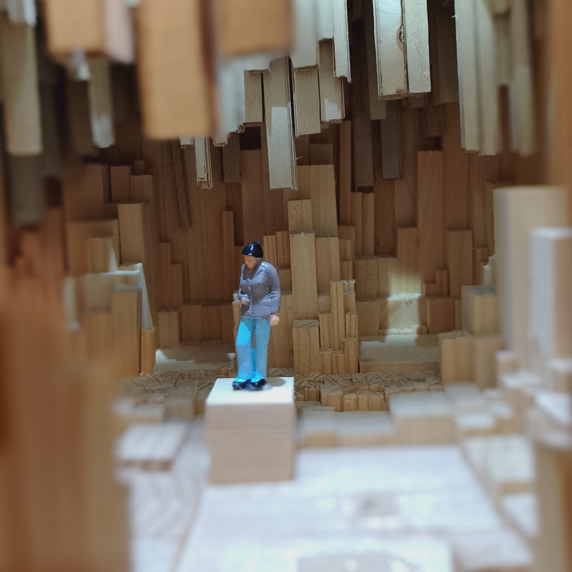 Eine Modellfigur auf einem Holzsockel in einem aus Holzstäben zusammengesetztem Innenraum